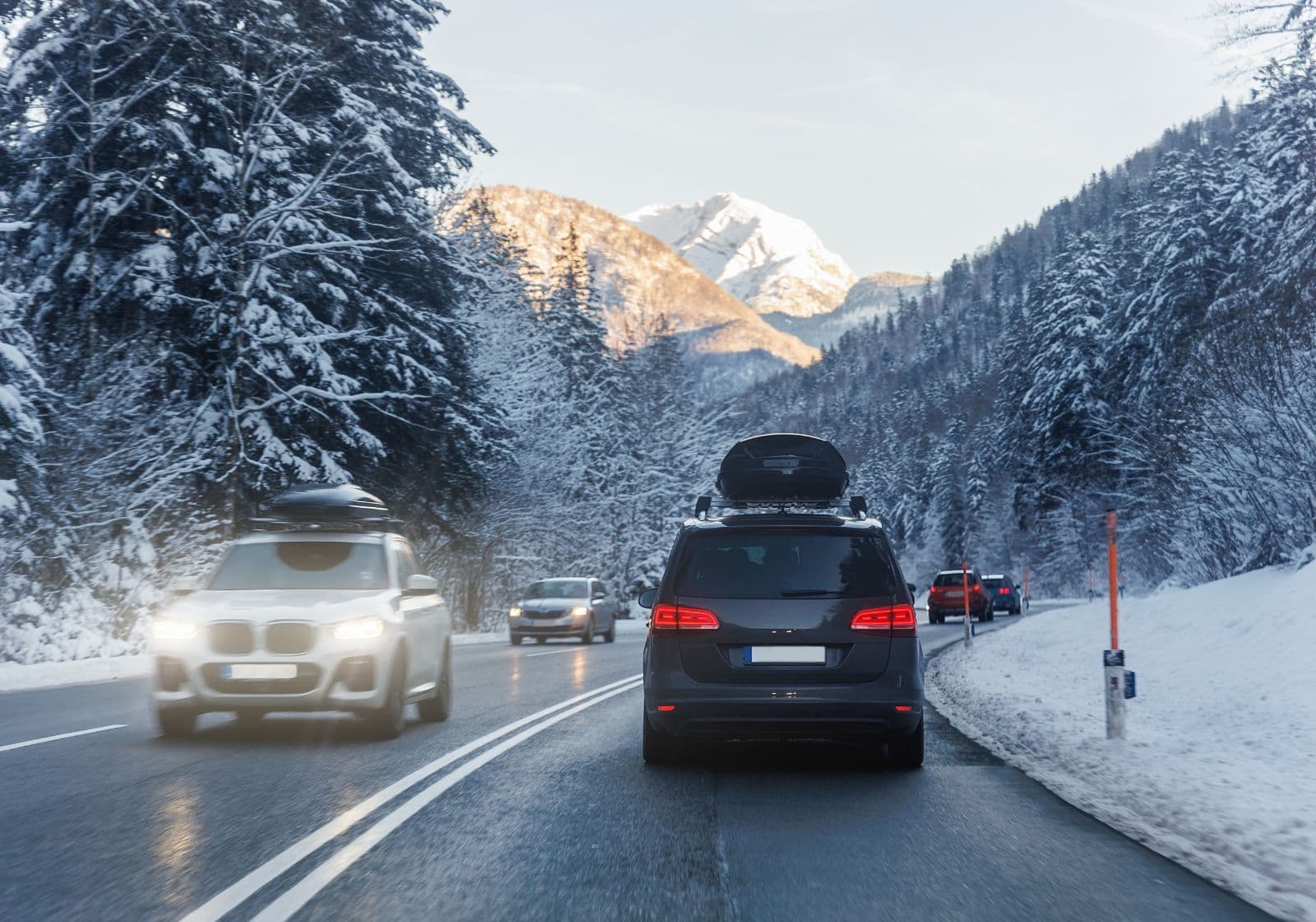Bil med tagboks kører på vej med sne på træer og bjergtoppe